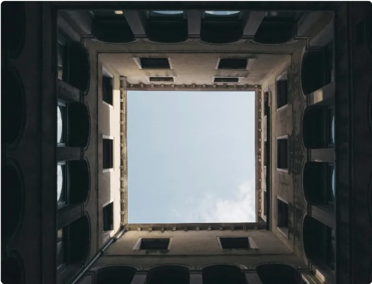Kare bir binanın ortasında bulunan avludan yukarı doğru bakarak çekilmiş bir fotoğraf